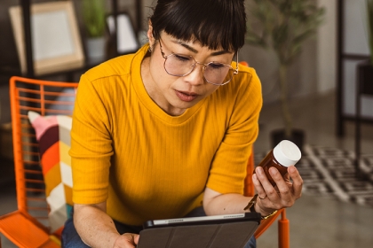 Woman in yellow shirt reading a supplement label and reading on an ipad